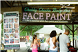 a woman stands under a sign advertising face painting