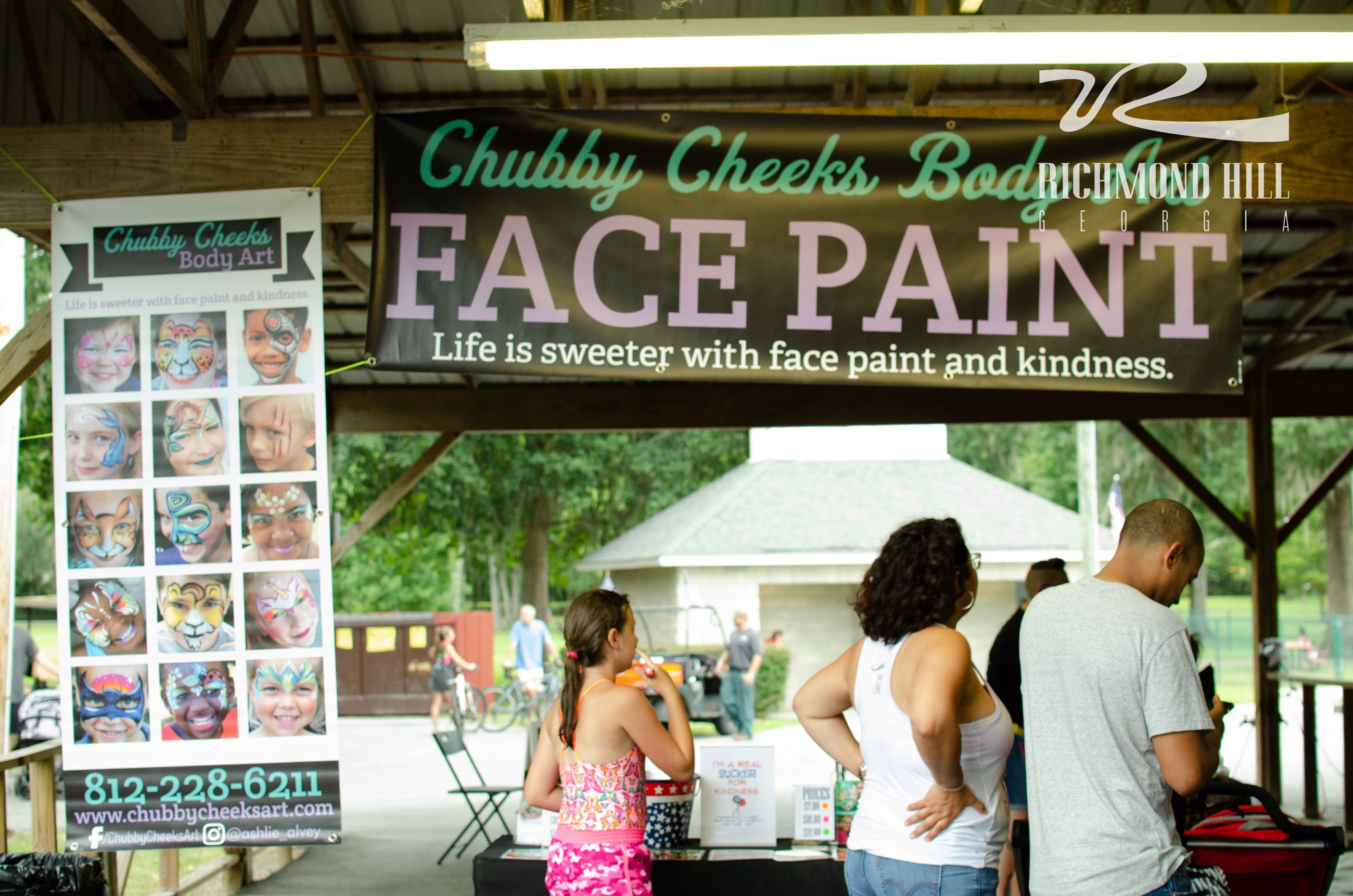 a woman stands under a sign advertising face painting
