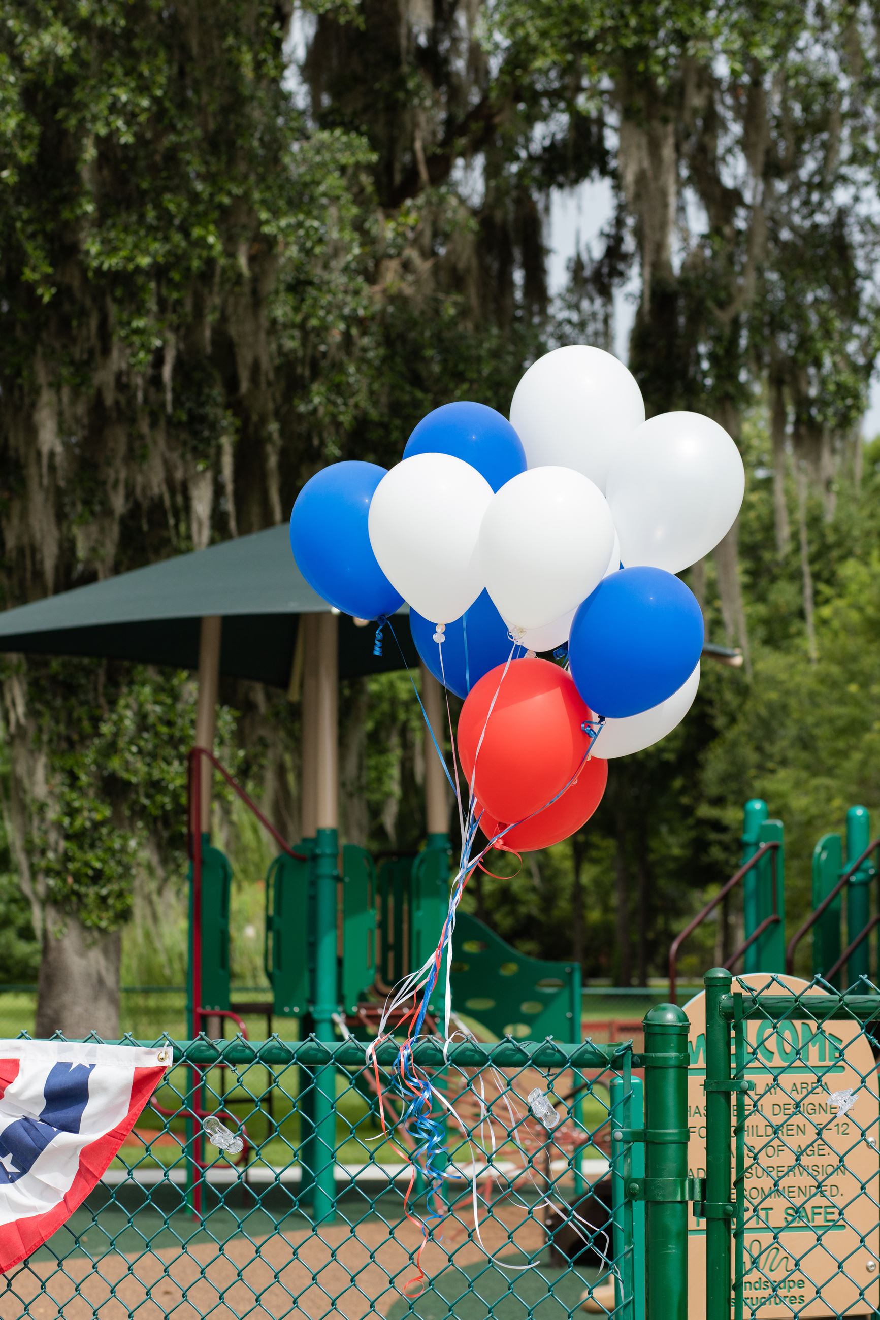 red white and blue balloons tied to playground fence